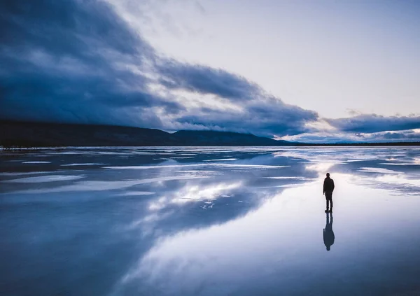 Lone Figure Stands Frozen Lake Reflection Storm Clouds — Zdjęcie stockowe