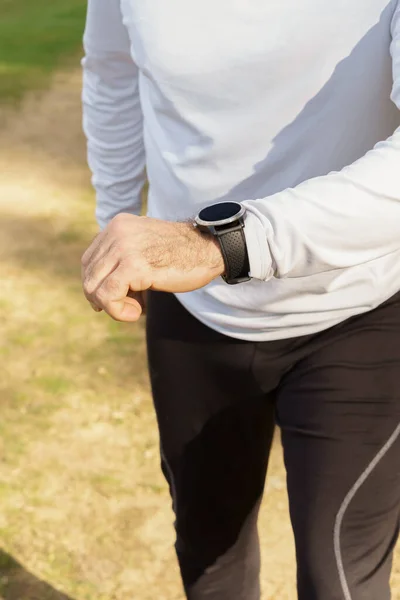 man training in the field with his smart watch wearing black pants and white t-shirt a pine forest in the background