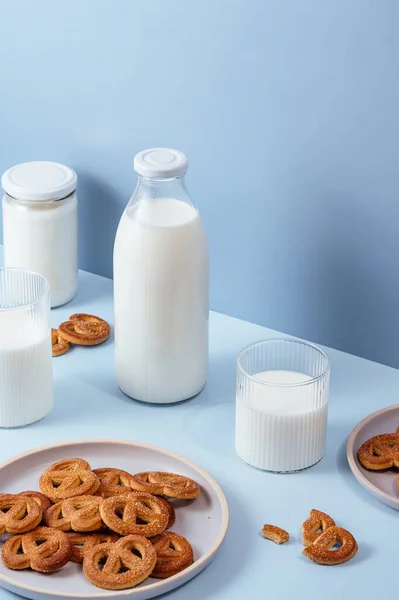 Milk in a glass and a bottle, cookies in a plate. Light blue background.