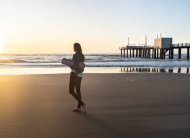 Beautiful woman walking at the beach at sunrise about to practice yoga
