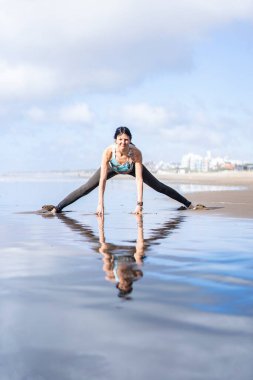 A woman doing stretching exercises at the beach while reflected on water
