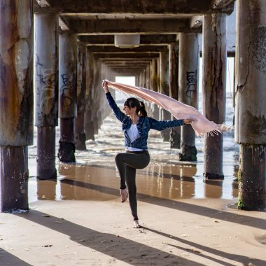 Woman dancing under a pier holding a scarf on the wind.