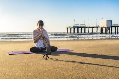 Slim woman yoga instructor giving online yoga training in a mobile phone camera. Yoga and meditation for social net.
