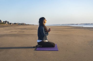 Side view of a woman sitting on the sand while meditating at the beach at sunrise