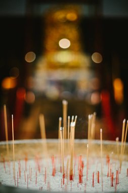 Incense sticks in sand alter in front of buddhist temple lights