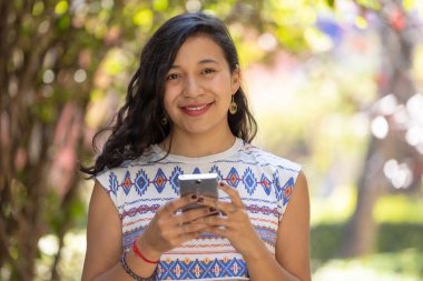 Real Mexican woman holding smart phone and looking at camera
