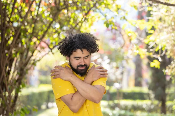 young Mexican man with beard and afro hugging himself, self love