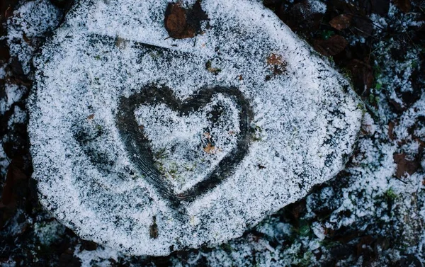 a love heart drawn into snow on a tree stump