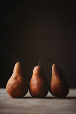 Close up of trio of brown pears shot against a dark background.