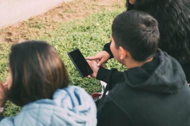 Arka gruptan Latinler akıllı telefonlarıyla parkta oturuyorlar.