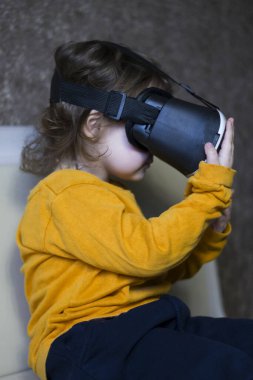 Küçük kız sanal gözlüklerle oyun oynuyor ve onlara dokunuyor.