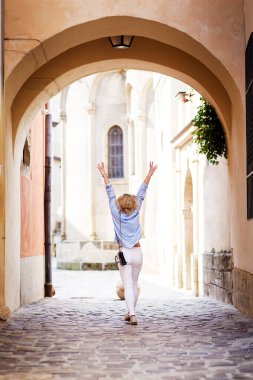 blonde woman in a blue shirt and light pants walks a summer town