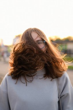 The wind blows the hair of a young woman at sunset