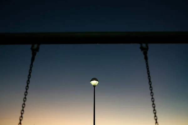 From below of old metal swing chain with glowing street light in background against cloudless sky at night in Reykjavik