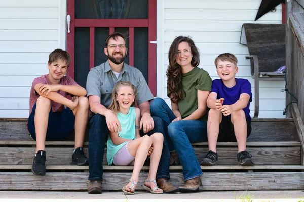 Happy family of five sitting on farmhouse steps.
