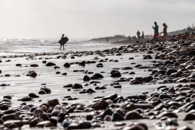 Arka planda suya giren insanların olduğu çakıl taşı plajı.