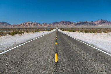 Long and straight road between mountains with blue and clear sky