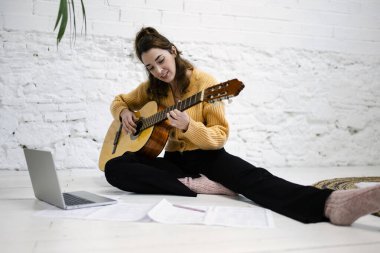 Beautiful young woman playing the guitar at home