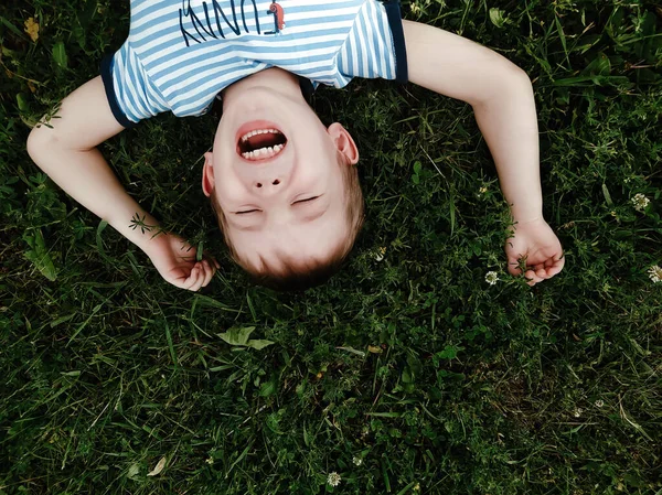 笑着的小男孩躺在外面的绿草上 — 图库照片