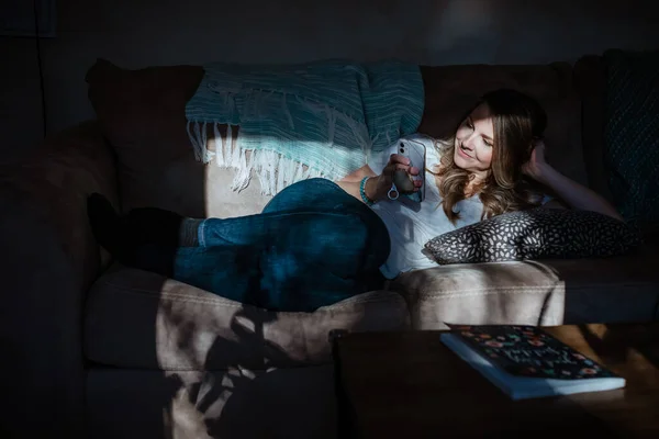 女人躺在沙发上看家里的手机 — 图库照片
