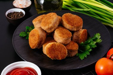 fried chicken nuggets on a black plate, ketchup in a saucepan, vegetables on a background nearby.