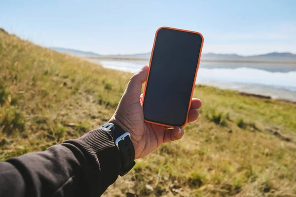 Close up of mobile phone in arms of man on blurred landscape