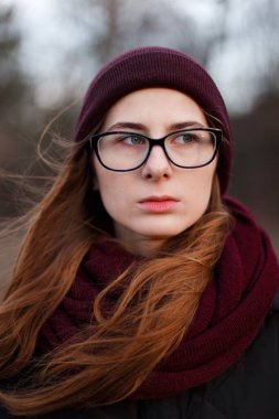 Parkın ortasında şapkalı, ceketli, kızıl saçlı bir kadın.