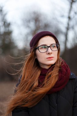 Parkın ortasında şapkalı, ceketli, kızıl saçlı bir kadın.