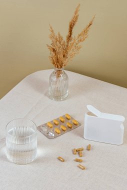 vitamins in capsules scattered on the table. a glass of water.