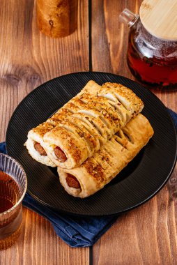 sausage in dough on a black plate on a wooden countertop