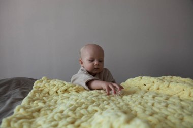 Çocuk, bej bir duvarın yanına bir çiçek ve sarı örülmüş bir battaniye alır.