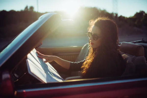 头发卷曲的女人在有太阳的老式汽车上看地图 — 图库照片