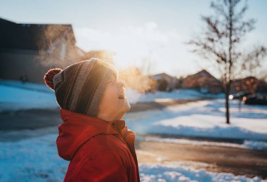 Kışın giyinmiş çocuk güneşli kış gününde soğuk havada gülüyor..