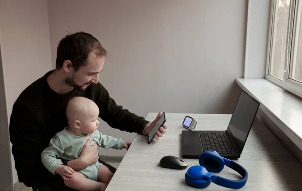 Father working at home on laptop with little child