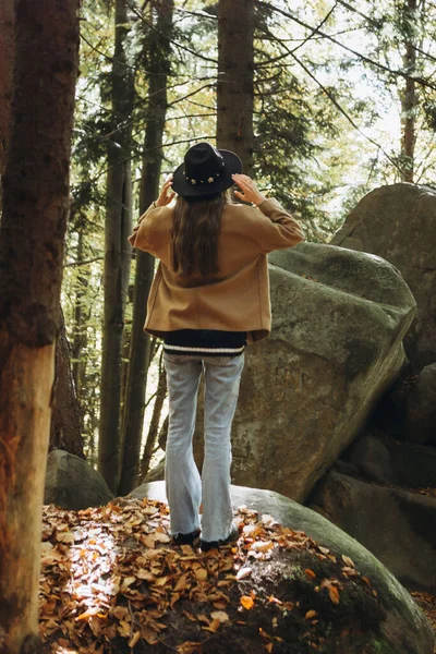 森林里穿着棕色夹克头戴黑色帽子的年轻女子 — 图库照片