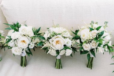 three wedding bouquets with all white flowers and greenery on linen