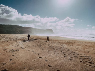 Geniş plajda, Nazare 'de kayalıkları olan koyu renk siluetler.