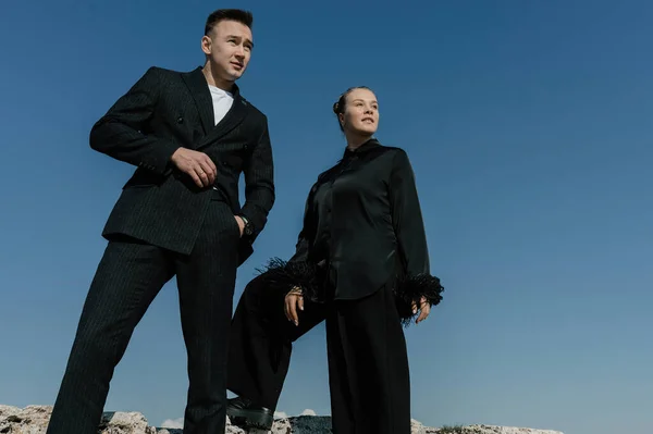 A man and a girl in black clothes stand against a blue cloudless sky