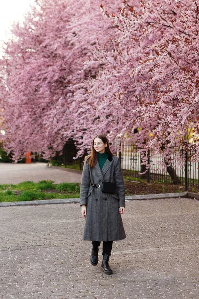 春になると毛布を着た若い女性が桜の間を歩き — ストック写真