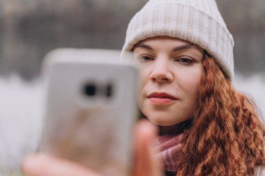 Kıvırcık saçlı, 30-35 yaşlarında, örgü şapkalı bir kadın telefonunu ciddiye alıyor.