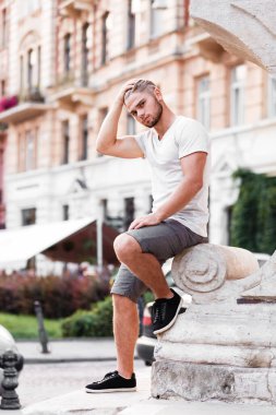 bearded blond man in a t-shirt and shorts on street of summer city