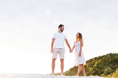 man and a woman are walking on a sandy beach in summer