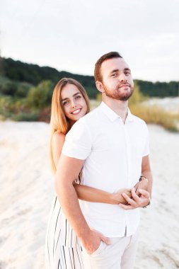 man and a woman are hugging on a sandy beach in summer