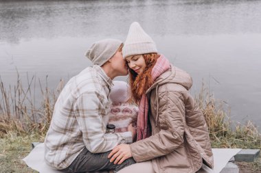 Nehir kenarındaki bir bahar parkındaki bankta çocuklu bir aile.