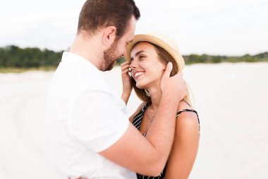 man and a woman are hugging on a sandy beach in summer