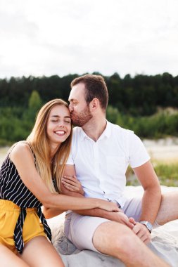 man and a woman are kissing and hugging on a sandy beach