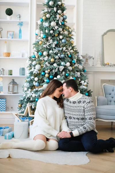 couple is hugging near a Christmas tree with gifts in a room