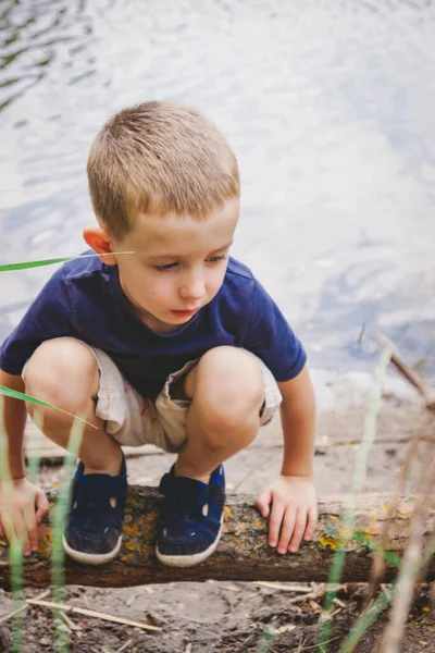 可悲的男孩正坐在河岸上的一根木头上 — 图库照片