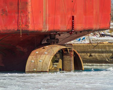 Sudaki kırmızı büyük bir geminin altındaki ahşap bir motorun yakın çekim görüntüsü.
