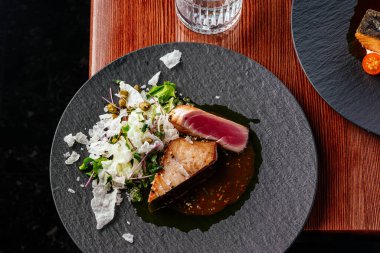 Ahşap bir masada soslu ızgara ton balığı bifteği.